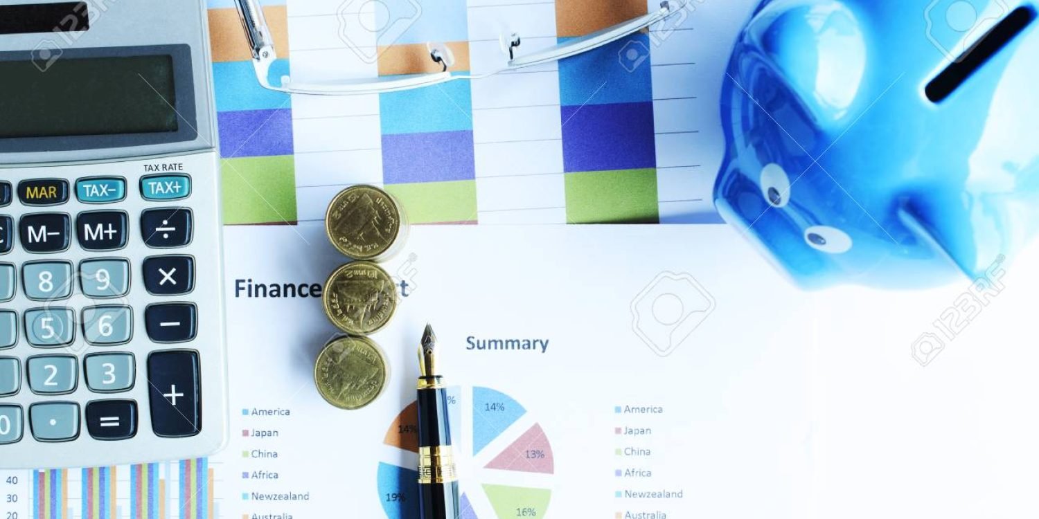 Financial concept with money coins stack and business fountain pen and calculator and eyeglasses and blue piggy bank labtop with document chart on desk office backgrounds above